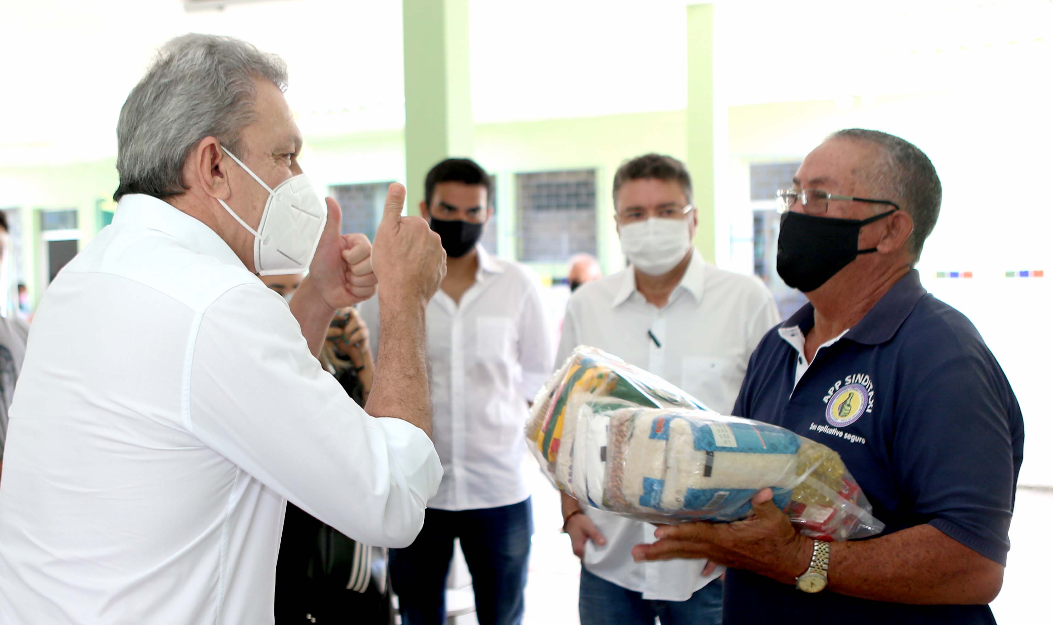 Sarto entrega uma cesta básica a um homem, ambos usam máscara